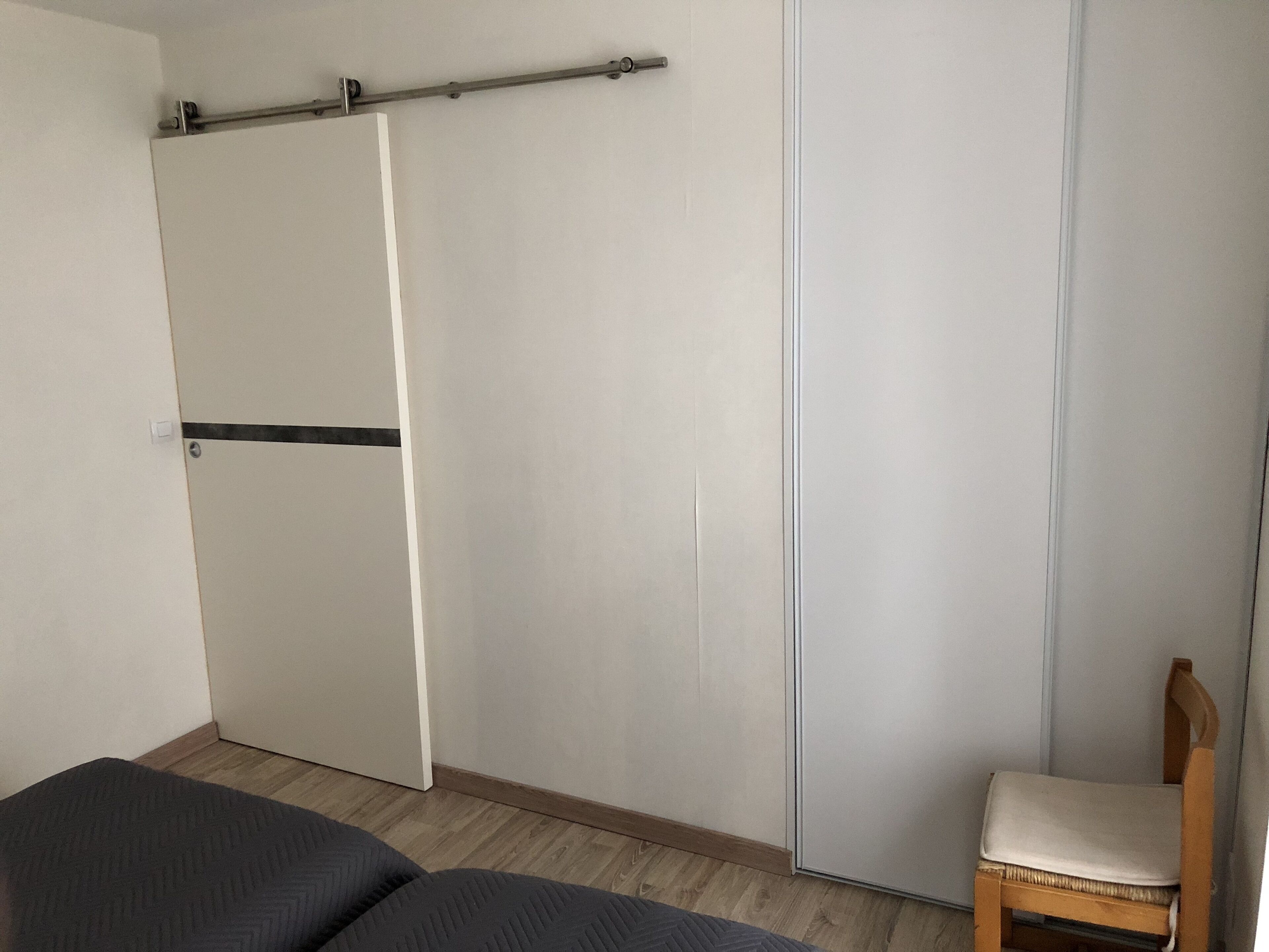 A bedroom with a bed, a wooden chair, and a wardrobe with a pull handle.
