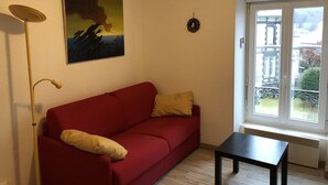 Um sofá vermelho com almofadas amarelas, uma mesa de centro preta, um candeeiro de chão e um quadro na parede.