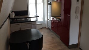 Cozinha compacta com mesa de jantar preta, armários brancos e uma parede com destaque em vermelho.