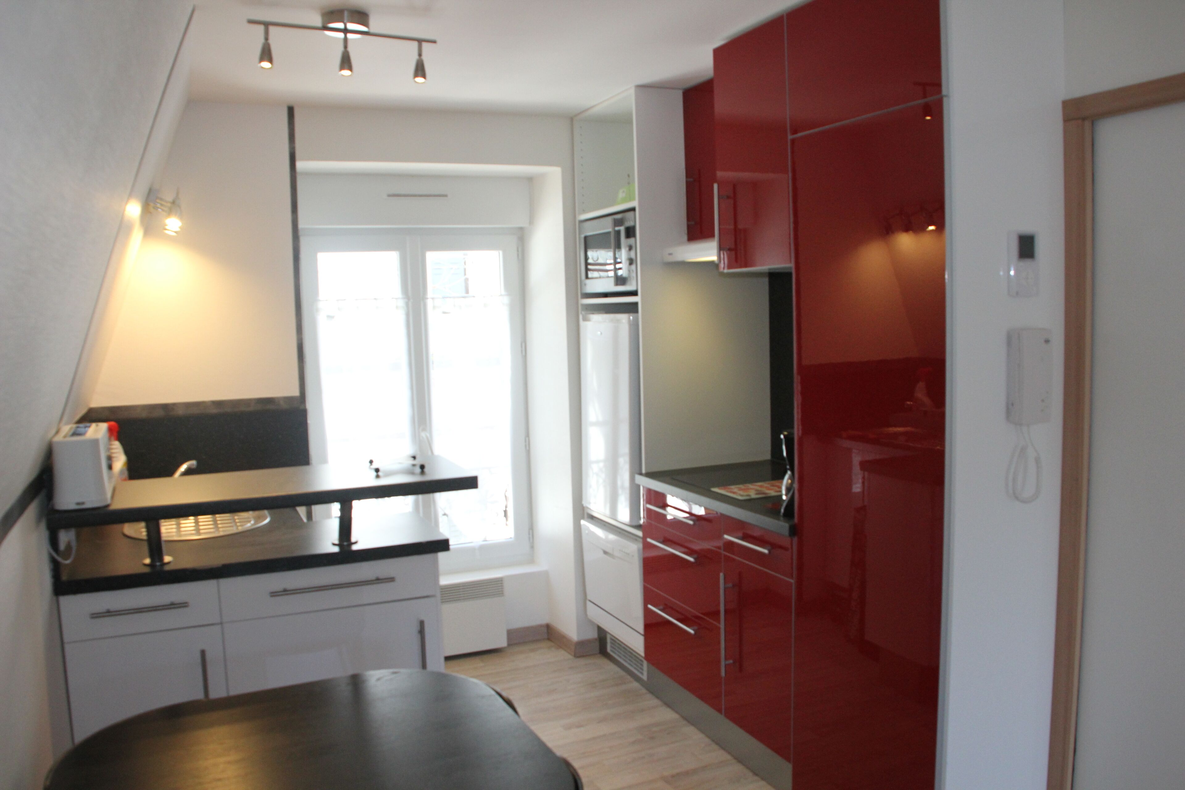 A compact kitchen with white and red cabinetry, a black countertop, and a window providing natural light.