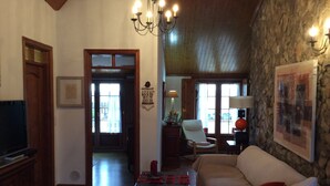A cozy living room with a stone wall, a wooden ceiling, a television, a sofa, a chair, and a table with a lamp. - Roof Top apartment, quiet, 2 large terraces, close to the best beaches (Lourinha)