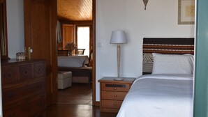 A bedroom with a wooden dresser, a bedside table with a lamp, a bed with a patterned headboard, and a view into the dining area. - Roof Top apartment, quiet, 2 large terraces, close to the best beaches (Lourinha)