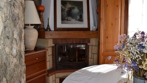 A fireplace with a framed picture above it, a stone wall, a wooden cabinet, and a vase of flowers. - Roof Top apartment, quiet, 2 large terraces, close to the best beaches (Lourinha)