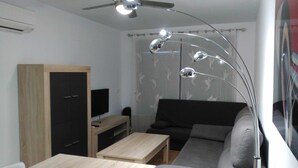 Un salon moderne comprenant un canapé, un téléviseur, une table en bois, un ventilateur de plafond et un miroir décoratif.