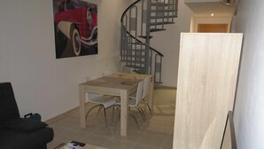 Un coin repas avec une table et des chaises en bois, un canapé noir et un escalier.