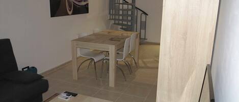 Un comedor con una mesa y sillas de madera, un sofá negro y una escalera.