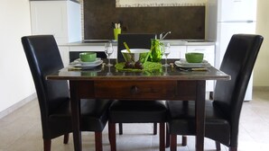 A dining area with a wooden table, black chairs, and a kitchen in the background. - CHARMING GUEST GARDEN TERRACE SWIMMING POOL, FREE PARKING AND WIFI, BEACHES 8 Km away  (Pomérols)