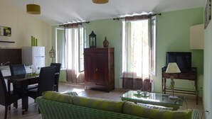 A living room with a sofa, dining table, and chairs. There is a cabinet, a television, and a lamp. - CHARMING GUEST GARDEN TERRACE SWIMMING POOL, FREE PARKING AND WIFI, BEACHES 8 Km away  (Pomérols)