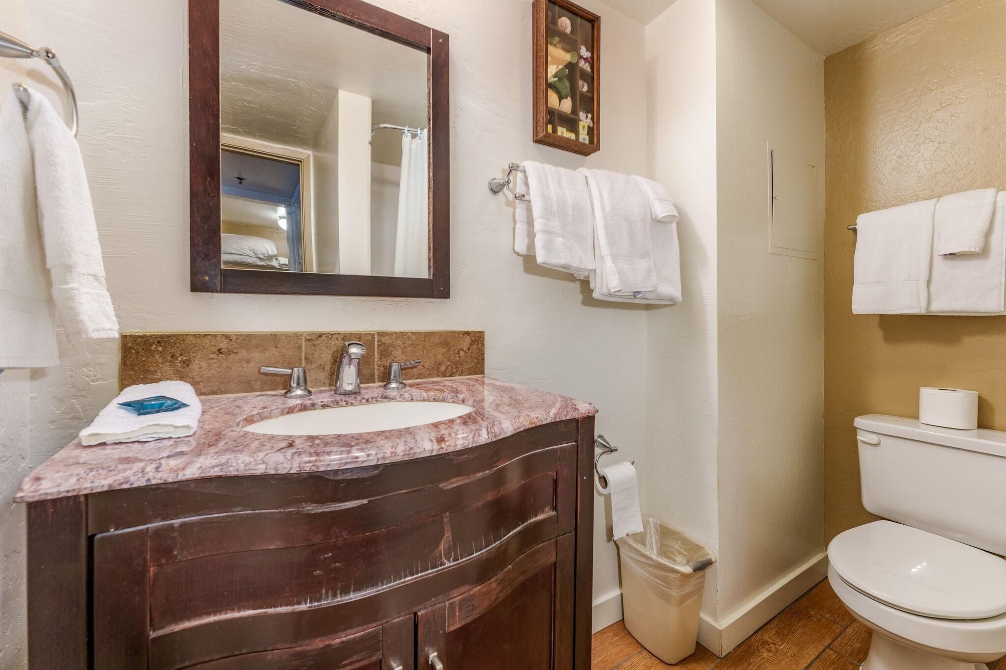 A bathroom with a marble sink, dark wooden vanity, white toilet, and a small trash bin.