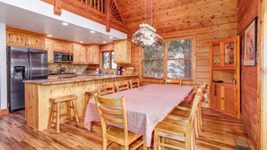 Una cabaña de madera con cocina que cuenta con una isla grande, taburetes de bar y una mesa de comedor preparada para seis personas.