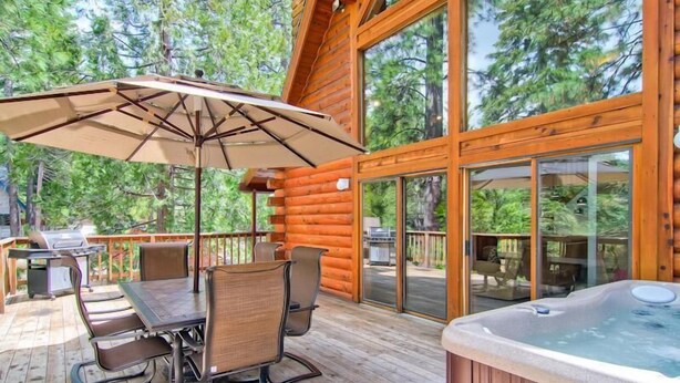 Una terraza de madera con un jacuzzi, una mesa con sillas y una sombrilla.