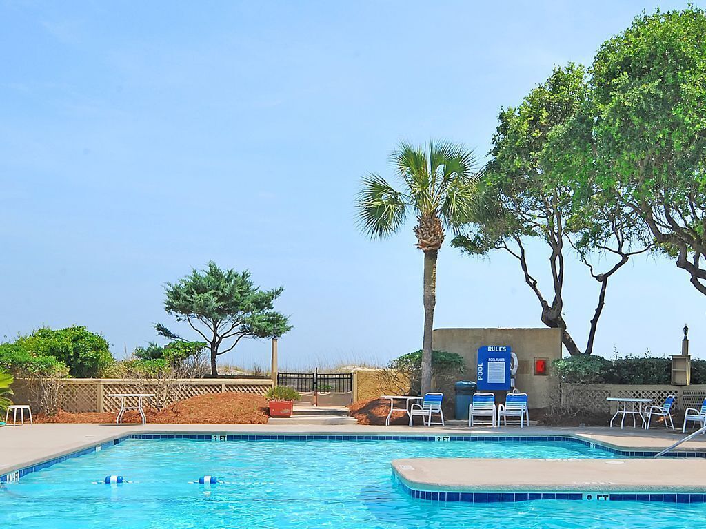 A swimming pool with lounge chairs and a sign indicating pool rules.