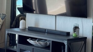 Un televisor de pantalla plana montado en la pared, sobre un mueble bajo de madera oscura, con un cuenco blanco y una botella verde.