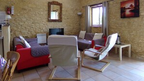 A living room with a stone wall, a red sofa, a white armchair, a TV, and a painting. - Pretty Dordogne valley house, heated swimming pool sleeps 8 (7 adults max) (Nadaillac de rouge)