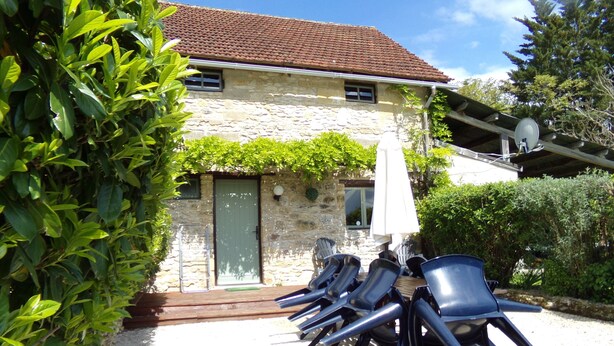 A stone building with a tiled roof, a door, and a window. There are several blue chairs and a white umbrella outside. - Pretty Dordogne valley house, heated swimming pool sleeps 8 (7 adults max) (Nadaillac de rouge)
