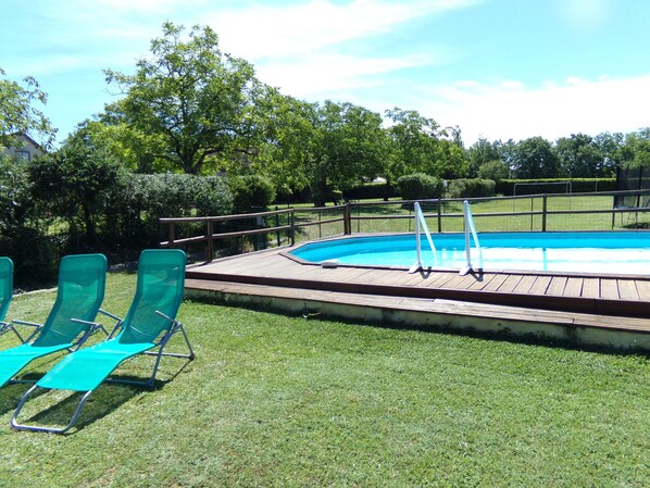 A swimming pool with a wooden deck and metal railings, surrounded by green grass and trees. - Pretty Dordogne valley house, heated swimming pool sleeps 8 (7 adults max) (Nadaillac de rouge)