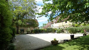 A courtyard with a gravel path, surrounded by greenery and buildings with traditional architecture. - Pretty Dordogne valley house, heated swimming pool sleeps 8 (7 adults max) (Nadaillac de rouge)