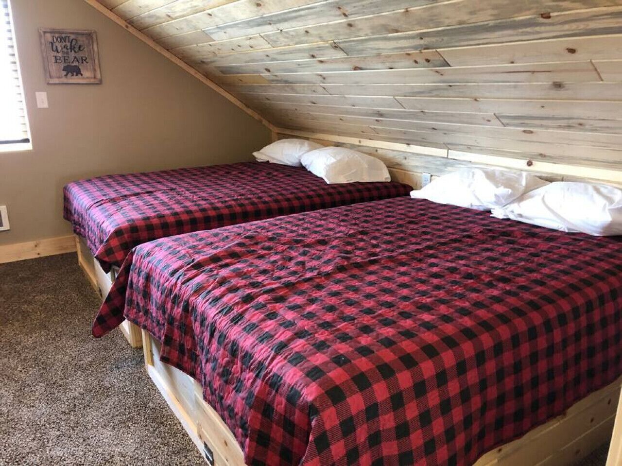 Una habitació amb dos llits, cada un amb un llençol a quadres vermells i negres.