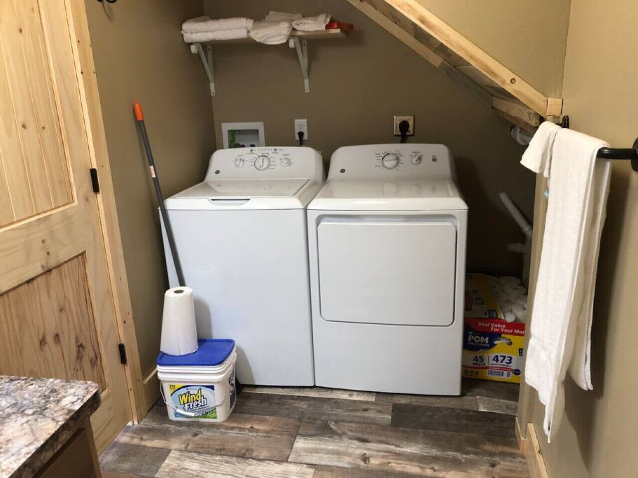 A laundry room with two white washing machines, a blue container labeled 'Wind-Fresh', and a roll of paper towels.