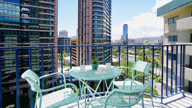 A balcony with a round table and two chairs, overlooking a cityscape with tall buildings. - 2-Bedroom Vacation Rental in Waikiki (Honolulu)