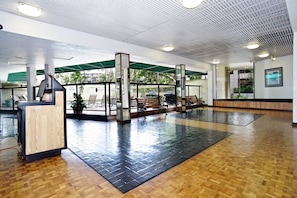 Un'ampia hall con una reception, zone salotto e un tendone verde che offre ombra.