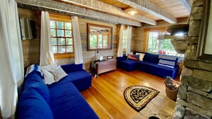 Ein gemütliches Wohnzimmer mit blauen Sofas, einem Kamin aus Stein und großen Fenstern.