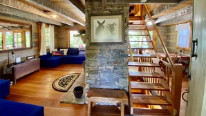 Ein rustikales Interieur mit Kamin aus Stein, Holzbalken, einem blauen Sofa und einer Treppe.