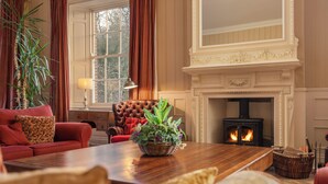 Un salon chaleureux avec une cheminée, un canapé rouge, une table basse en bois et une grande fenêtre.