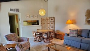 Ett vardagsrum med en soffa, fåtöljer, ett soffbord, ett matbord med stolar, en lampa och en dekorativ väggdekoration.