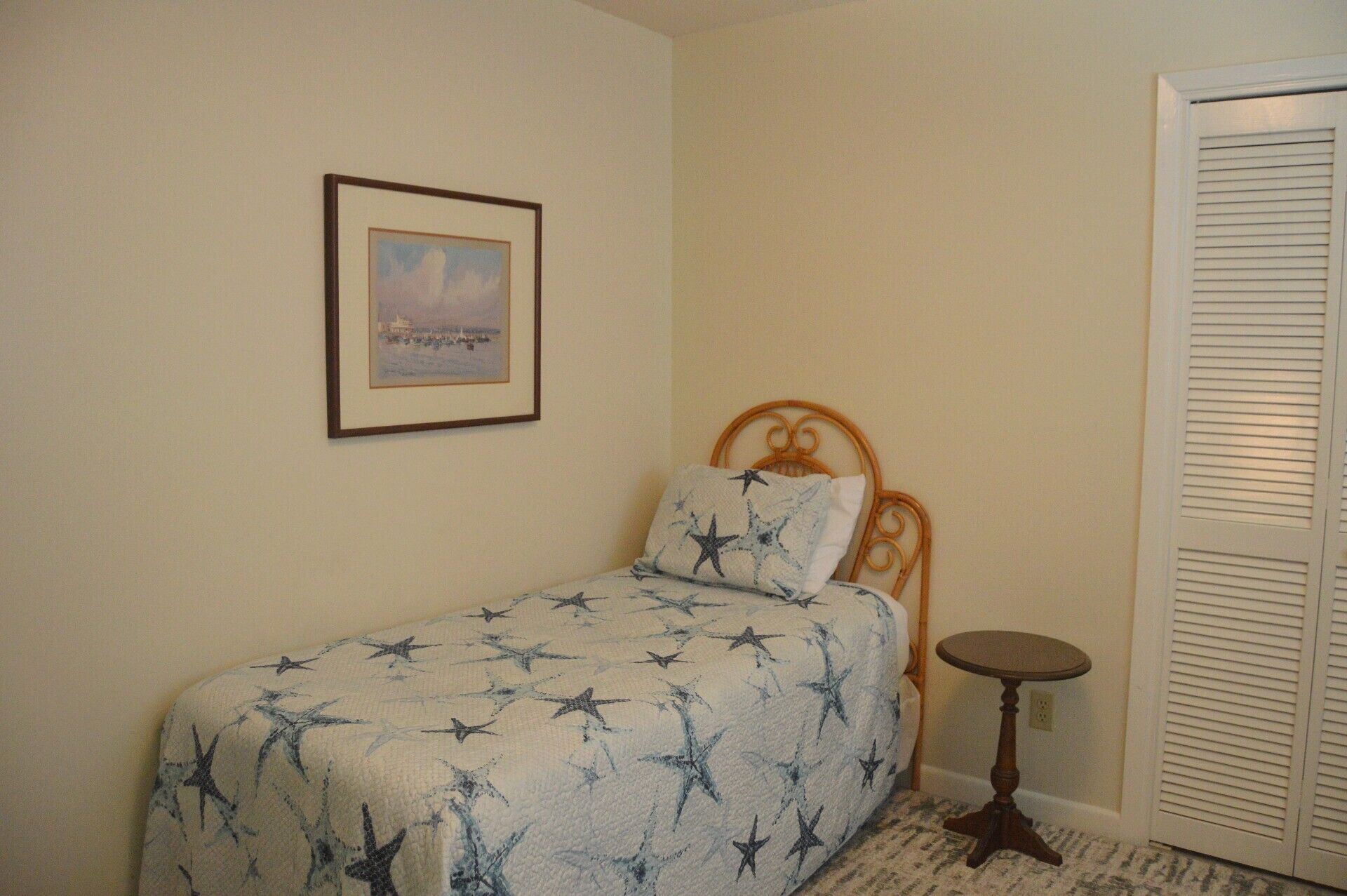 Un dormitorio con cama, una mesita redonda pequeña, un cuadro en la pared y una puerta con persianas.