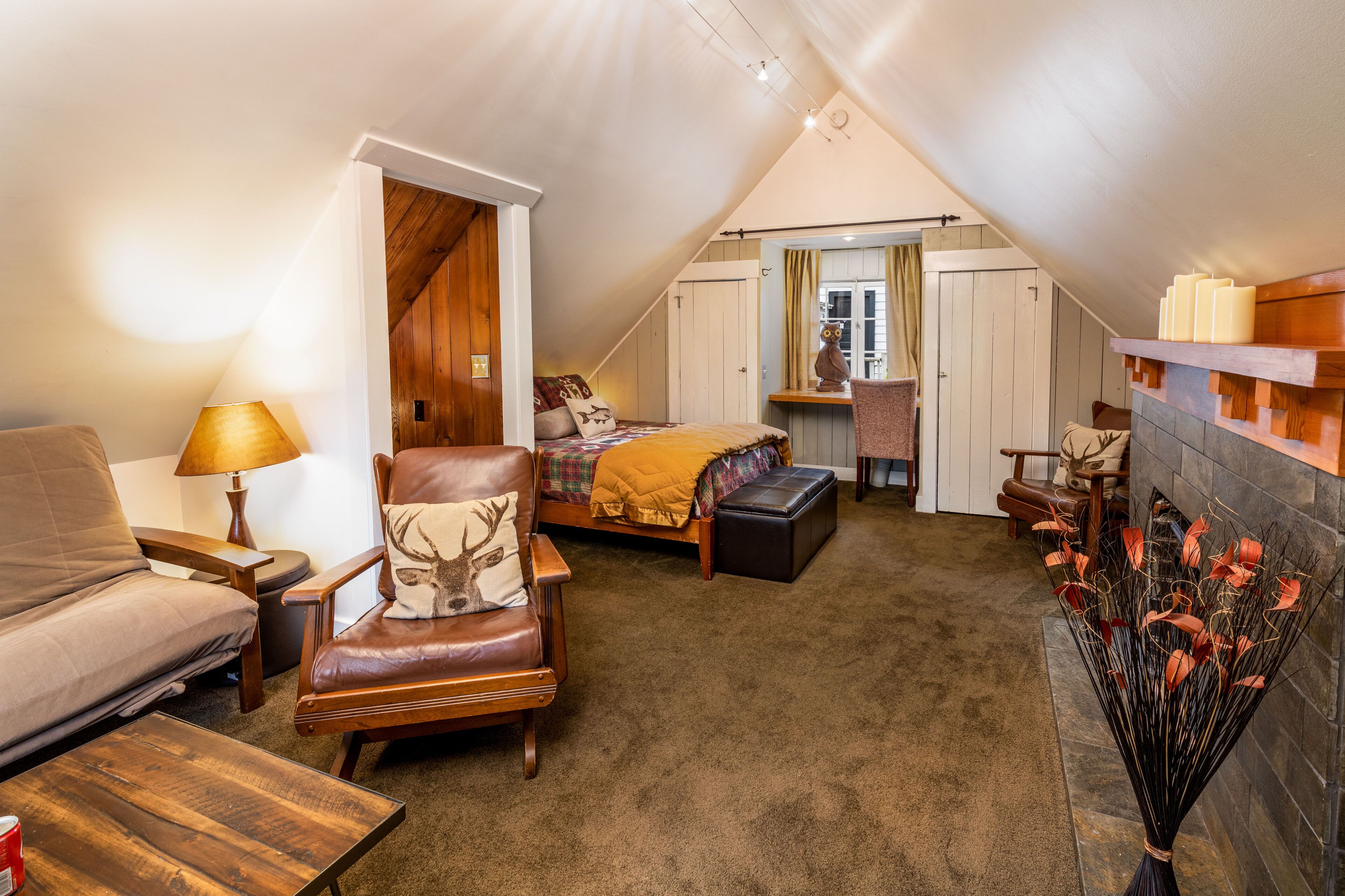 Een gezellige slaapkamer op zolder met een bed, een leren fauteuil, een bank, een open haard en uitzicht.