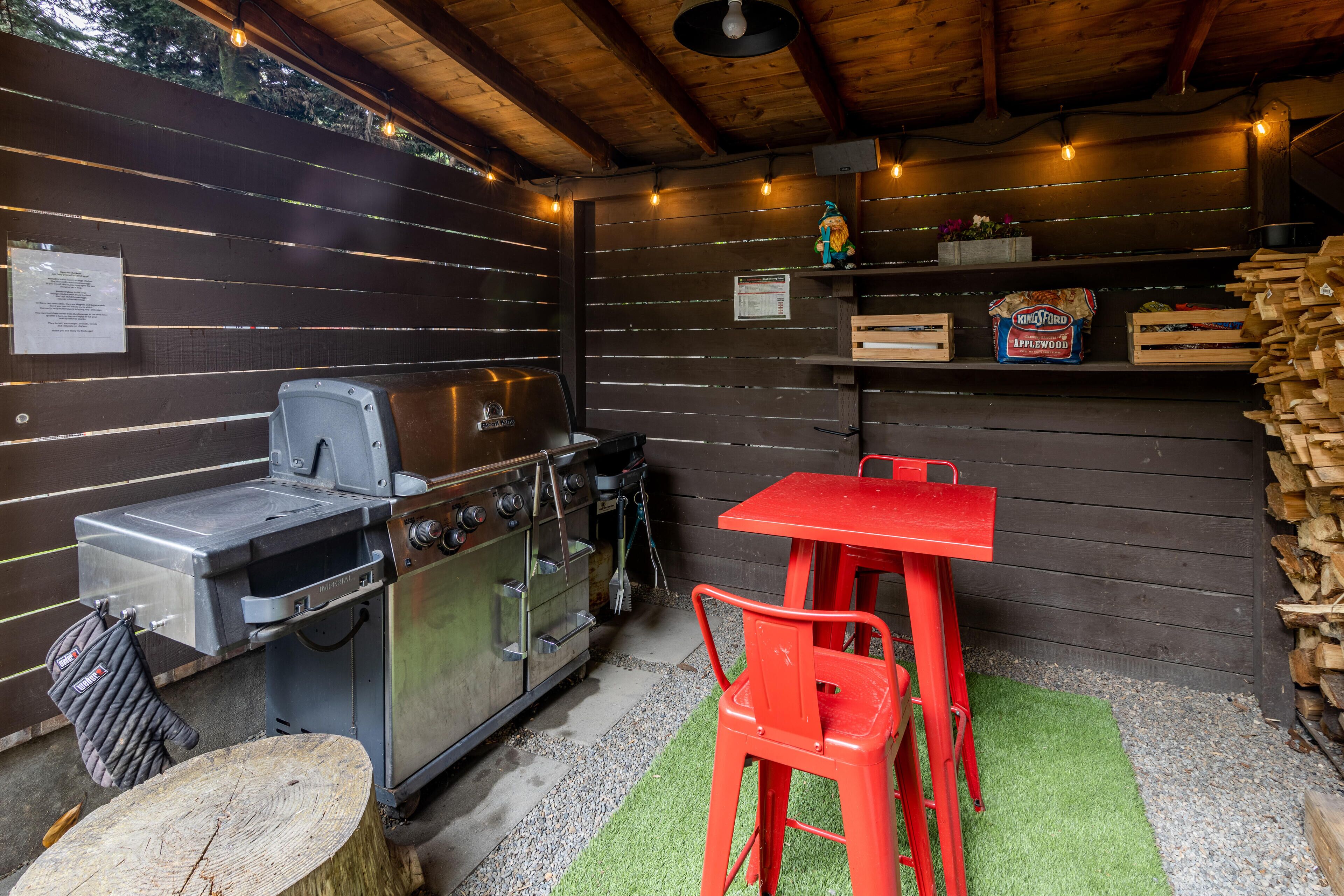 Un área de cocina al aire libre con una parrilla, una estufa y un juego de mesa y sillas rojas.