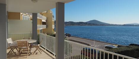 A balcony with a table and chairs, overlooking a body of water and a distant mountain.