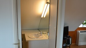 A room with a wooden floor, a white door, a white sink with a mirror, a television, and an air conditioner. - Gite d'OrAppart. for rent 1,400  (Vouvray)