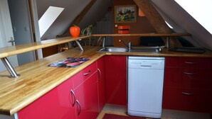 A compact kitchen with red cabinets, a white dishwasher, and a wooden countertop. - Gite d'OrAppart. for rent 1,400  (Vouvray)