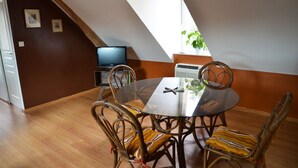 A dining area with a glass table and wicker chairs, a television, and a window with a plant. - Gite d'OrAppart. for rent 1,400  (Vouvray)