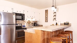 A modern kitchen with stainless steel appliances, a wooden island with bar stools, and a 'WELCOME' sign. - Ski View 9 - In Town - On Main Street - NEW Master Bedroom King Bed with New Mem (Red River)