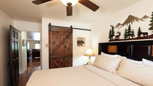A bedroom with a large bed, a wooden door, a ceiling fan, and a wall-mounted lamp. - Ski View 9 - In Town - On Main Street - NEW Master Bedroom King Bed with New Mem (Red River)