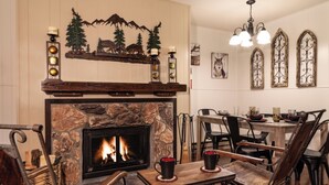 A cozy living room with a stone fireplace, wooden furniture, and a dining area with a chandelier. - Ski View 9 - In Town - On Main Street - NEW Master Bedroom King Bed with New Mem (Red River)
