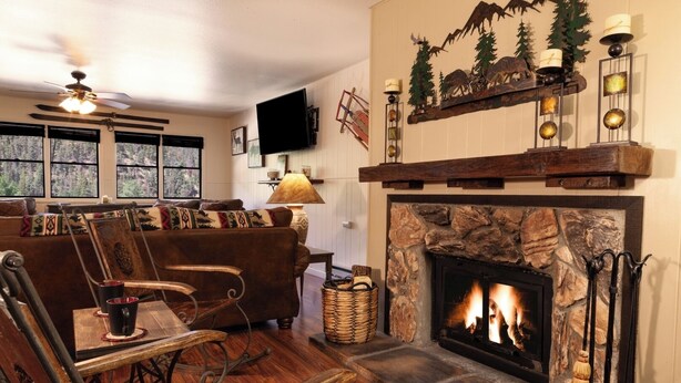 A cozy living room with a stone fireplace, wooden furniture, and a television mounted on the wall. - Ski View 9 - In Town - On Main Street - NEW Master Bedroom King Bed with New Mem (Red River)