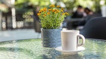 Una mesa de vidrio con una taza y platillo blancos, y un florero azul con flores amarillas.