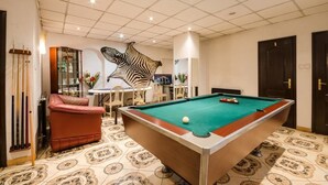 A pool table in a room with patterned floor tiles, a red leather chair, and a zebra mural on the wall. - Richter Pansion (Budapest)