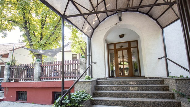 A building entrance with a covered porch, steps leading up to a door, and a fence with plants. - Richter Pansion (Budapest)
