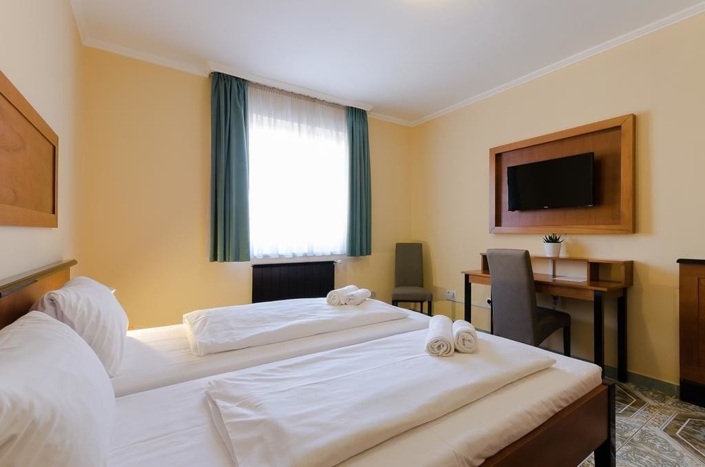 Habitación de hotel con dos camas, un escritorio, una silla, un televisor y una ventana con cortinas.