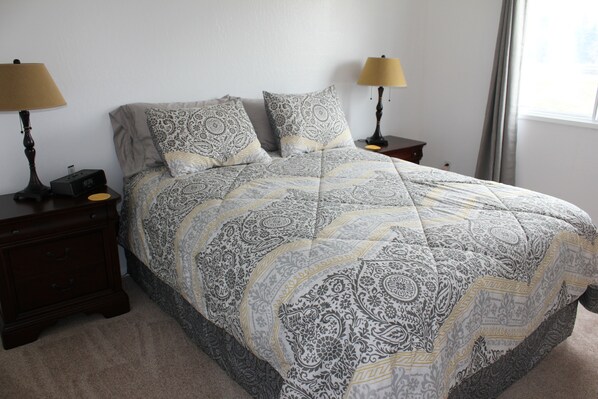 A bedroom with a large bed, two bedside tables, two lamps, and a window with curtains. - Bright End Unit Apartment (Anchorage)