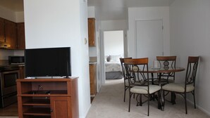 Ett kompakt bostadsutrymme med en matplats, ett litet kök och en tv som står på ett träställ.