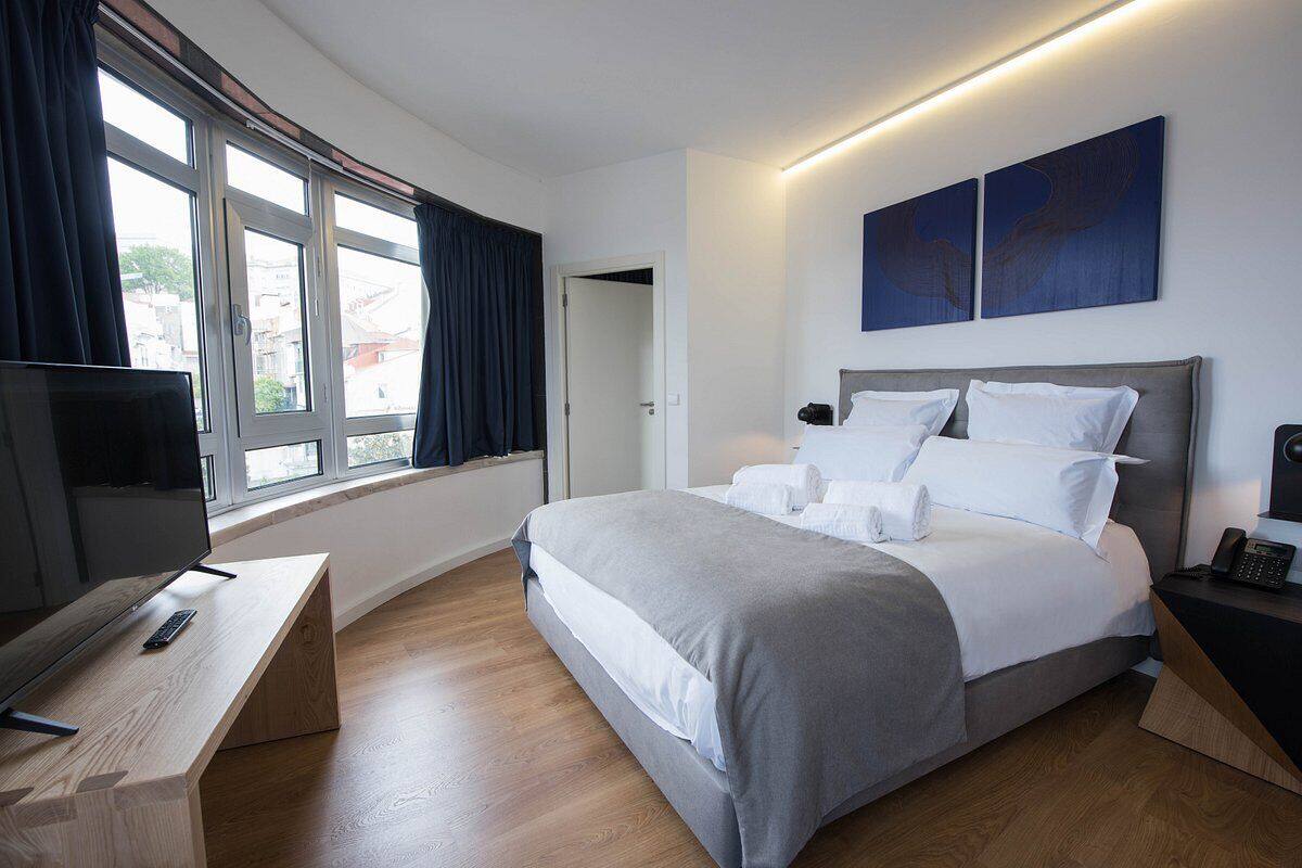 Una habitación de hotel moderna con una cama grande, un escritorio con televisor y vistas a la ciudad a través de amplias ventanas.