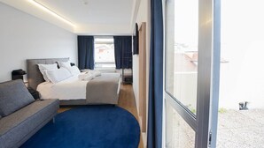 Una habitación de hotel moderna con una cama grande, un sofá, un escritorio y vistas a través de un ventanal.