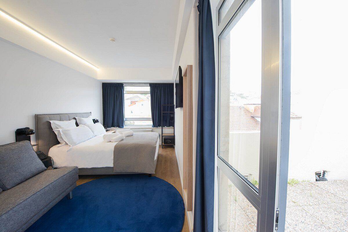 Una habitación de hotel moderna con una cama grande, un sofá, un escritorio y vistas a través de un ventanal.