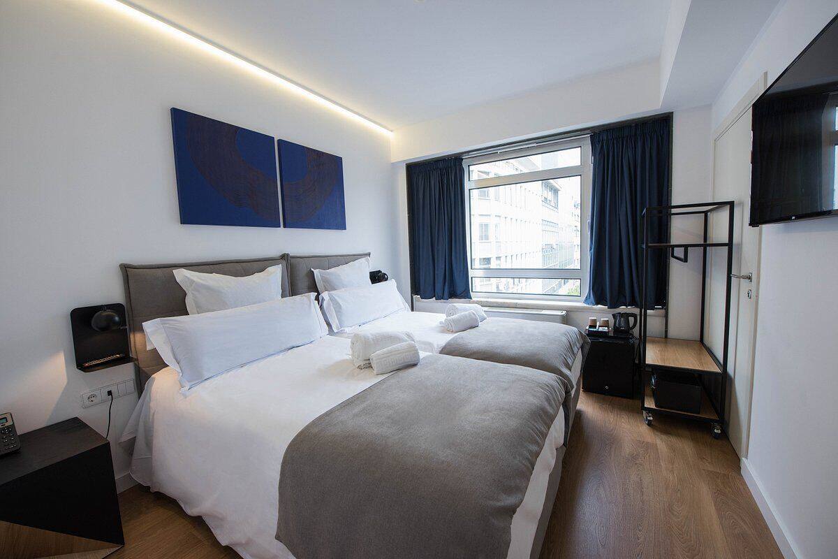 Una habitación de hotel moderna con dos camas, un escritorio, una silla, un televisor y una ventana con cortinas.